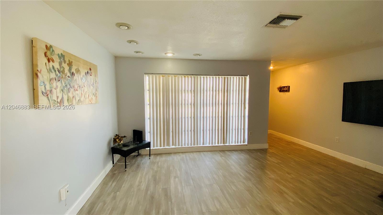 A living room features light wood-look flooring, a large window with vertical blinds, and recessed lighting — 6810 NW 28th St, Sunrise FL 33313, SUNRISE, FL