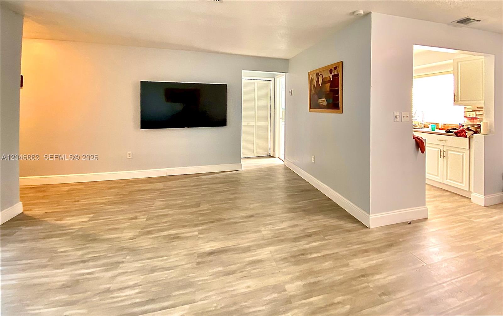 A living room with light wood-look flooring, a wall-mounted television, and an adjacent kitchen — 6810 NW 28th St, Sunrise FL 33313, SUNRISE, FL