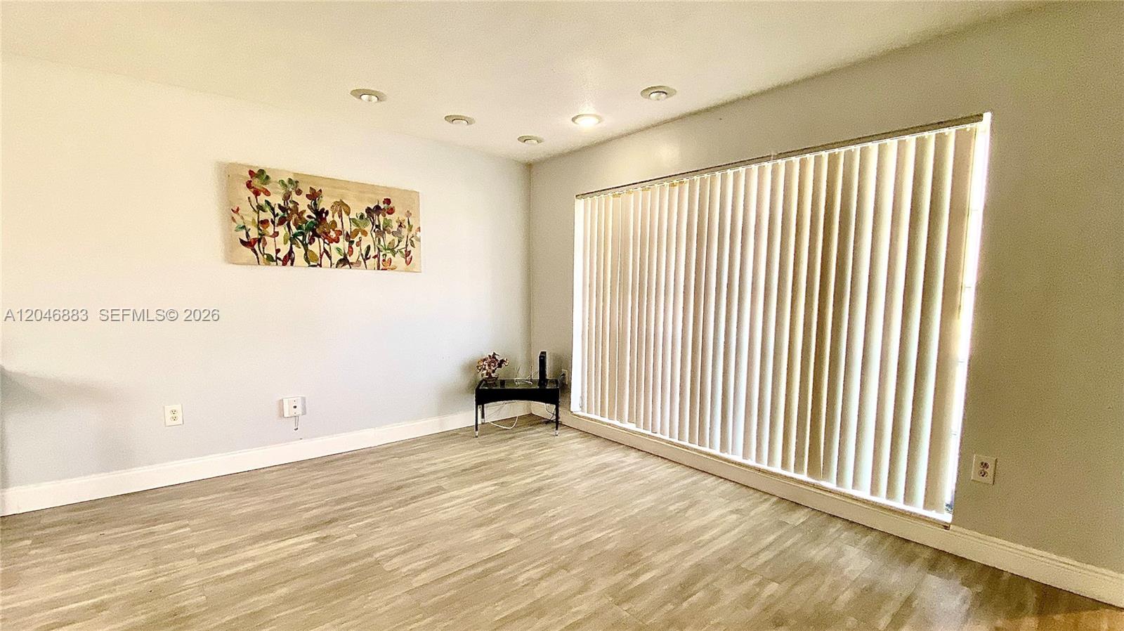 A room with light-colored walls, wood-look flooring, recessed lighting, and a large window with blinds — 6810 NW 28th St, Sunrise FL 33313, SUNRISE, FL