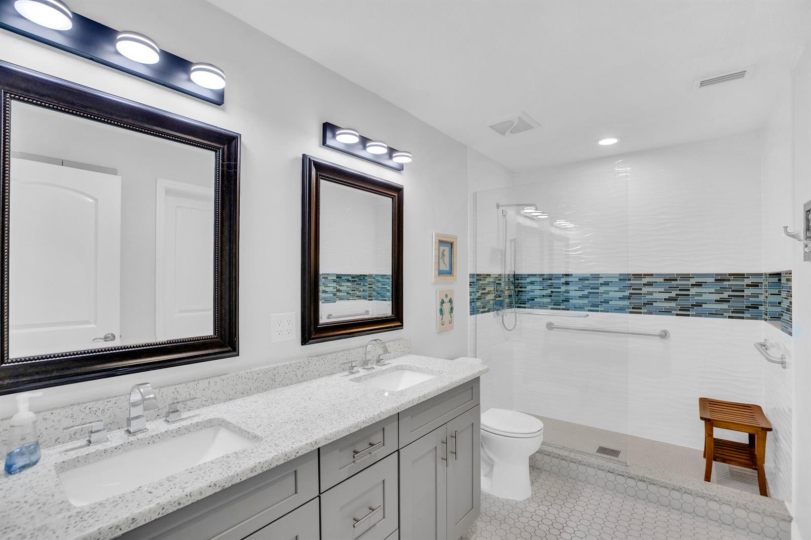 A bathroom features a double vanity with granite countertops, gray cabinets, and a walk-in shower — SEBASTIAN, FL
