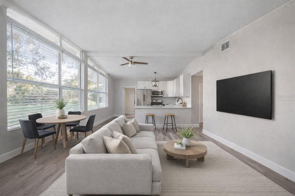 A living room and kitchen area with light wood flooring, a sofa, and large windows — 34796 GARDENIA WAY, DADE CITY, FL