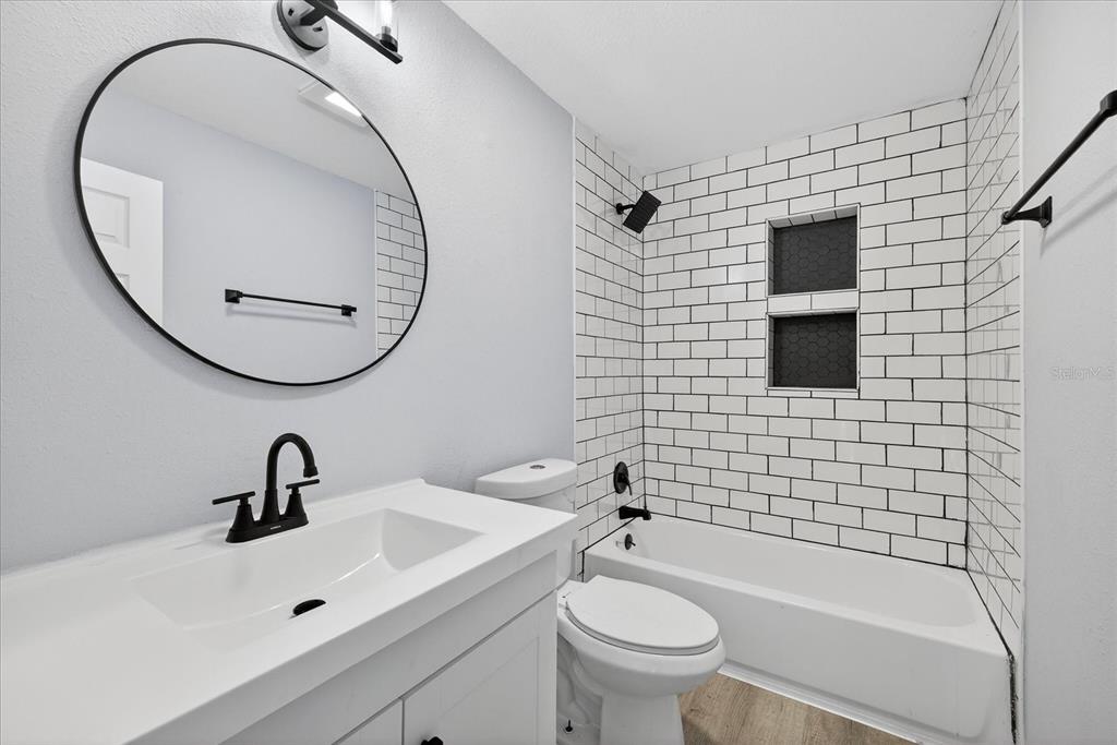 A modern bathroom features a white vanity, a round mirror, and a subway-tiled shower area — 34796 GARDENIA WAY, DADE CITY, FL