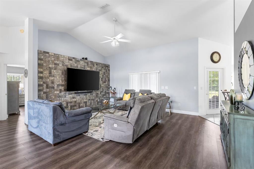 A living room features a stone accent wall, a large television, and gray furniture — 10360 SW 48TH AVENUE, OCALA, FL