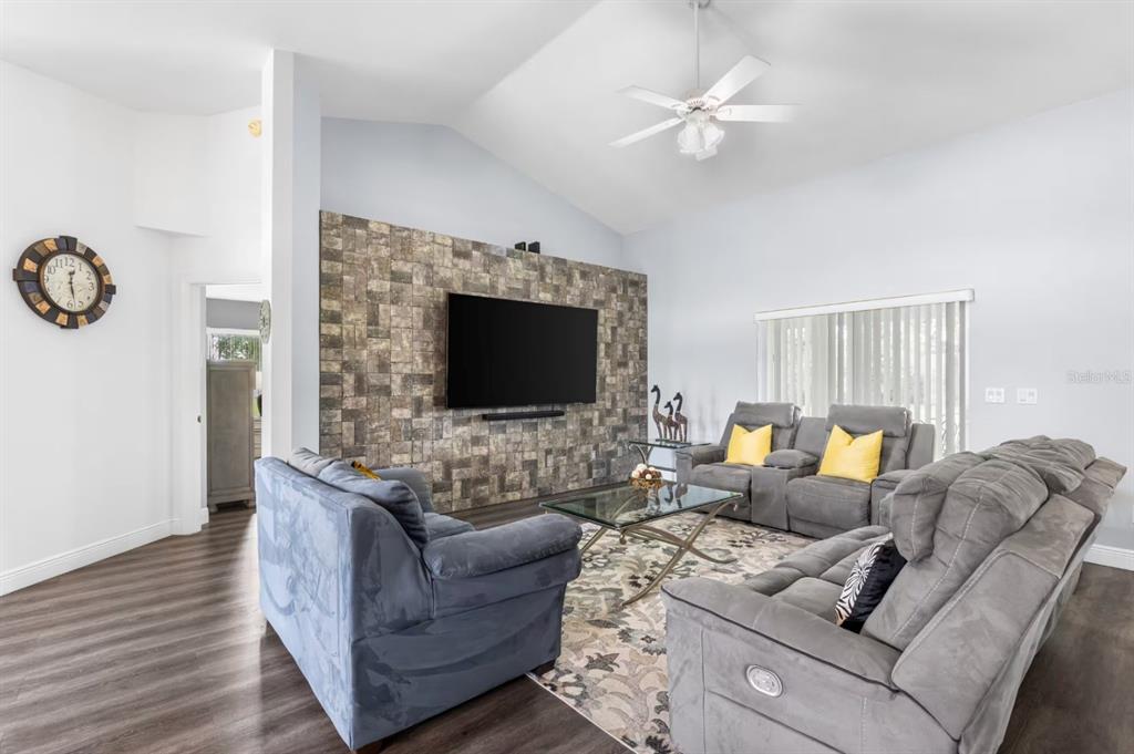 A living room features a stone accent wall with a mounted television and grey furniture — 10360 SW 48TH AVENUE, OCALA, FL