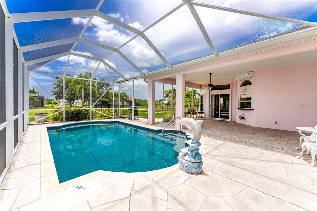 A screened-in patio features a swimming pool, a dolphin fountain, and light-colored stone pavers — 417 SCARLET SAGE, PUNTA GORDA, FL