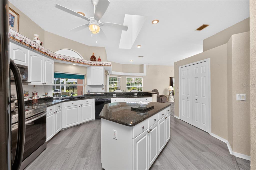 A kitchen with white cabinets, dark granite countertops, a central island, and wood-look flooring — 417 SCARLET SAGE, PUNTA GORDA, FL