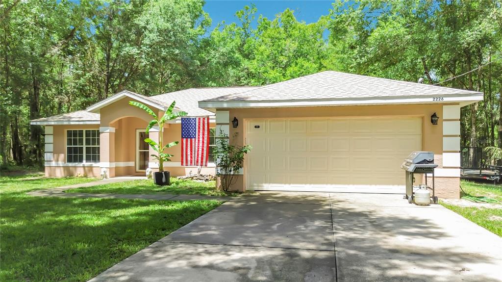 A single-story house with a beige exterior, a two-car garage, and an American flag — 2226 SW ALGIERS COURT, DUNNELLON, FL