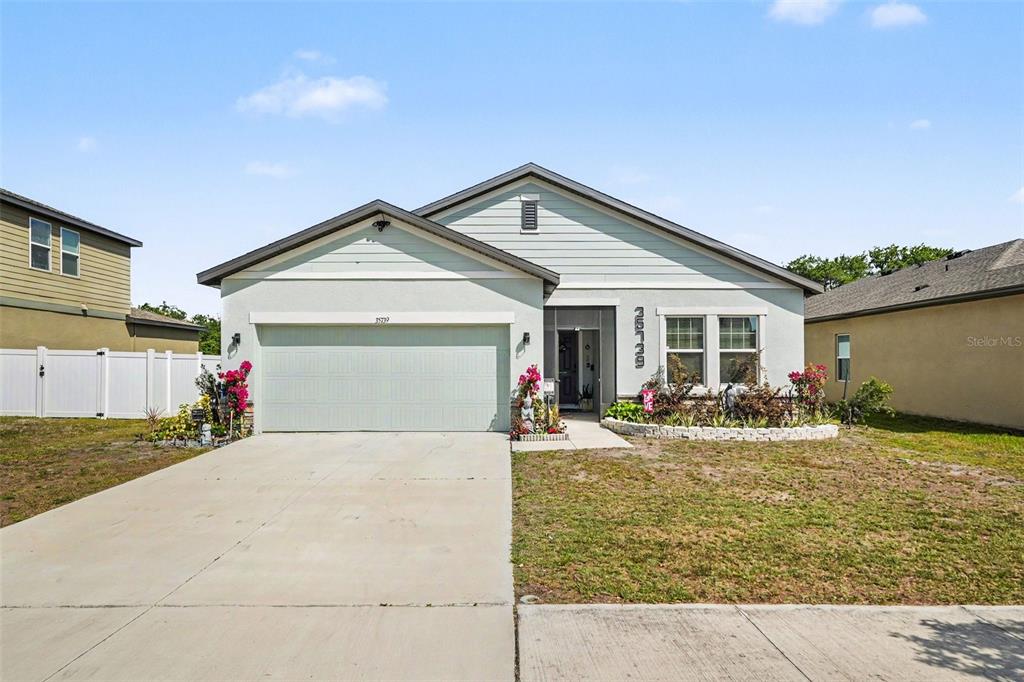 A single-story house with a light green exterior, two-car garage, and a front garden — 35739 BUTTONWEED TRAIL, ZEPHYRHILLS, FL