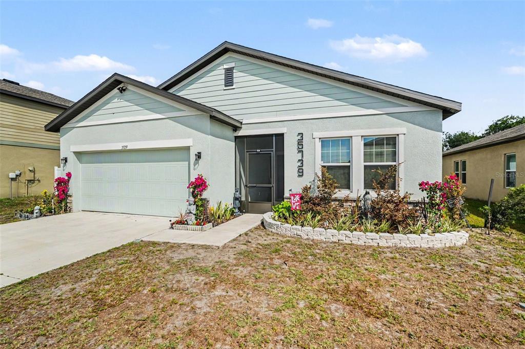 A single-story house with a light green exterior, a two-car garage, and a landscaped front yard — 35739 BUTTONWEED TRAIL, ZEPHYRHILLS, FL