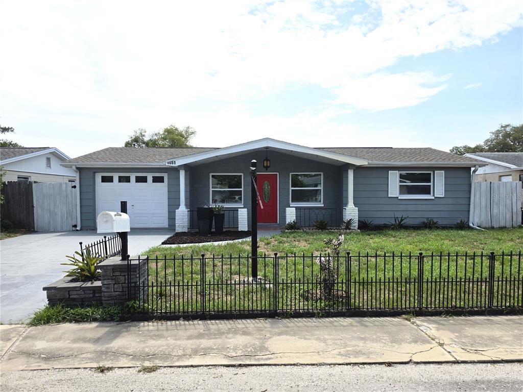 A single-story gray house with a red front door and a black metal fence — 1051 MAYBURY DRIVE, HOLIDAY, FL