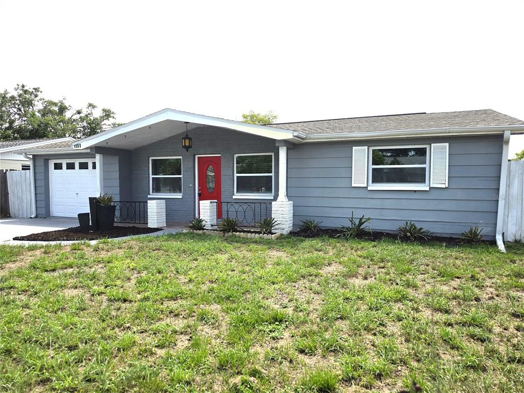 A single-story house with gray siding, a red front door, and a white garage door — 1051 MAYBURY DRIVE, HOLIDAY, FL