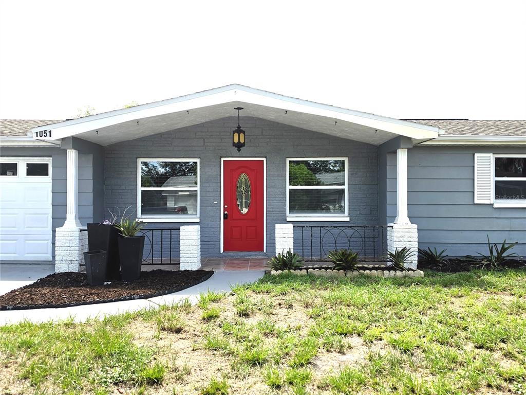 A gray house exterior features a bright red front door and a covered porch area — 1051 MAYBURY DRIVE, HOLIDAY, FL