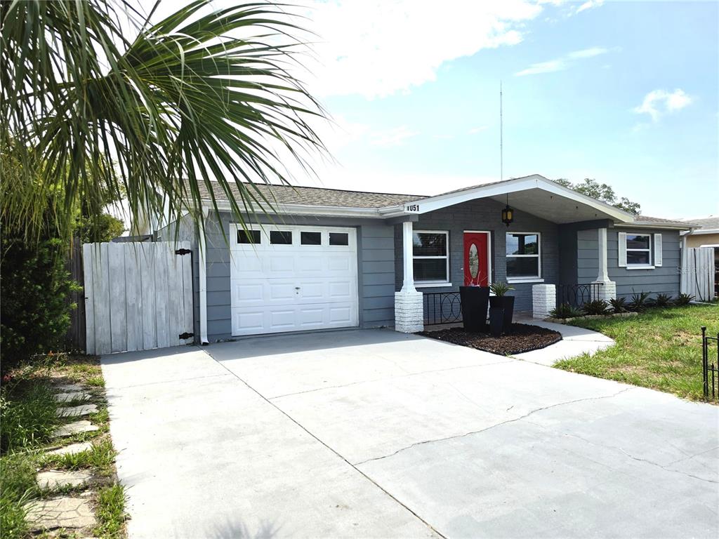 A single-story house with a gray exterior, a white garage door, and a red front door — 1051 MAYBURY DRIVE, HOLIDAY, FL