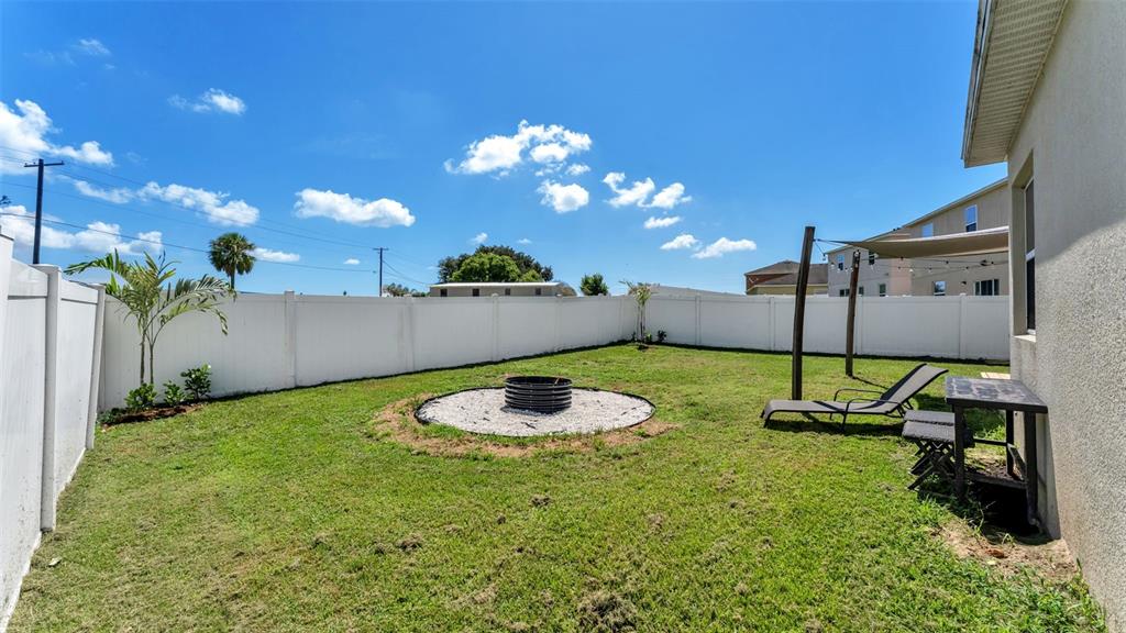 A fenced backyard features a circular fire pit area, a lounge chair, and a small table — 5798 DORNICH DRIVE, AUBURNDALE, FL
