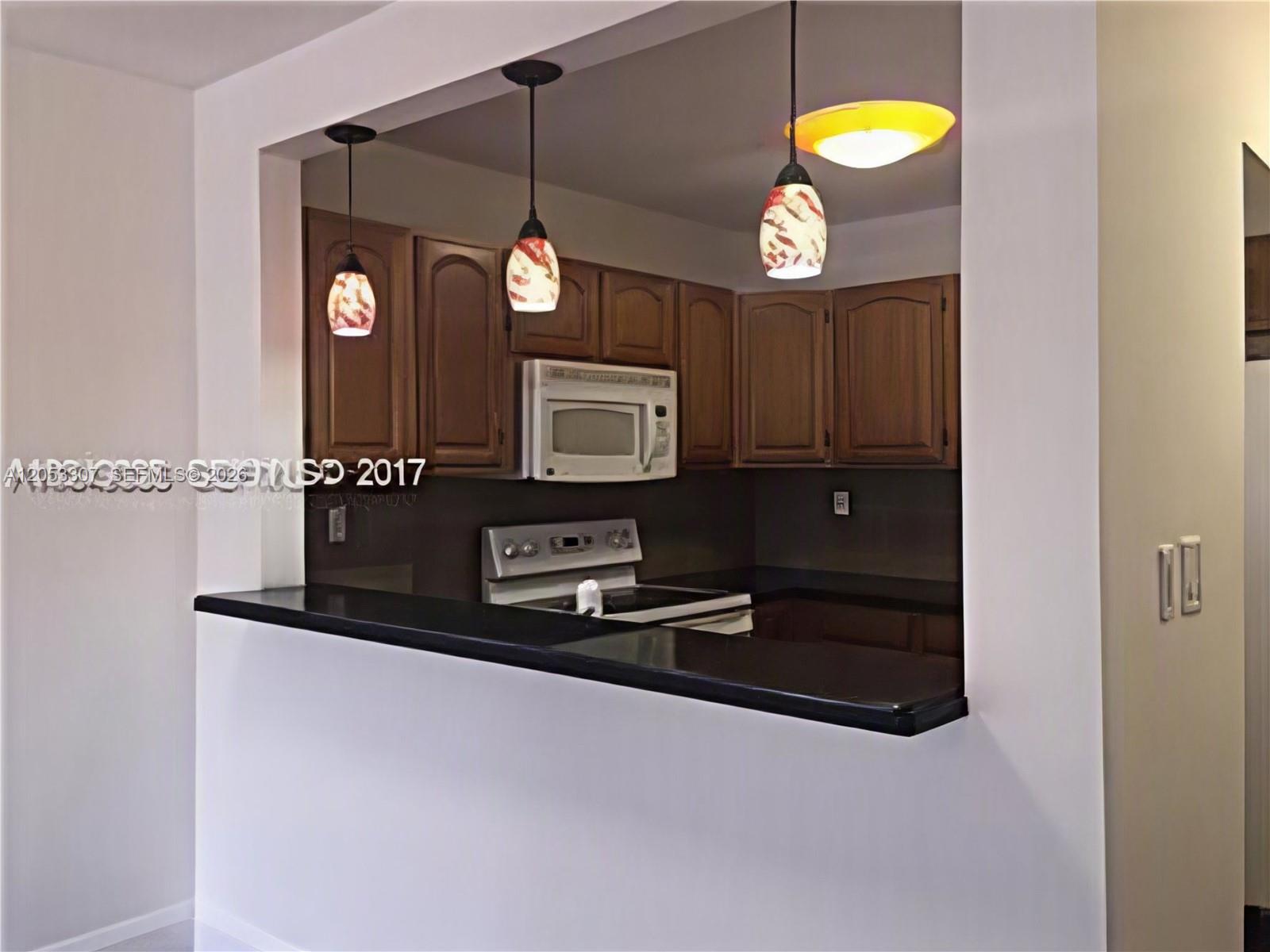 A kitchen with dark wood cabinets, black countertops, and three pendant lights over a counter — 8185 NW 7th St. # 101, Miami FL 33126, MIAMI, FL