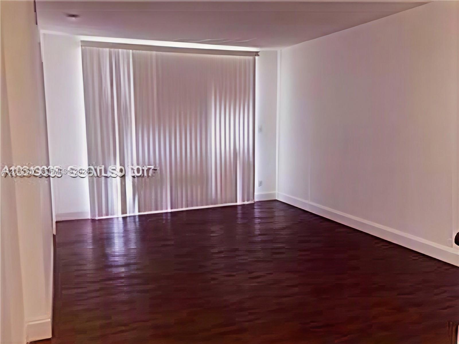 An empty room features dark wood flooring, white walls, and floor-to-ceiling vertical blinds — 8185 NW 7th St. # 101, Miami FL 33126, MIAMI, FL