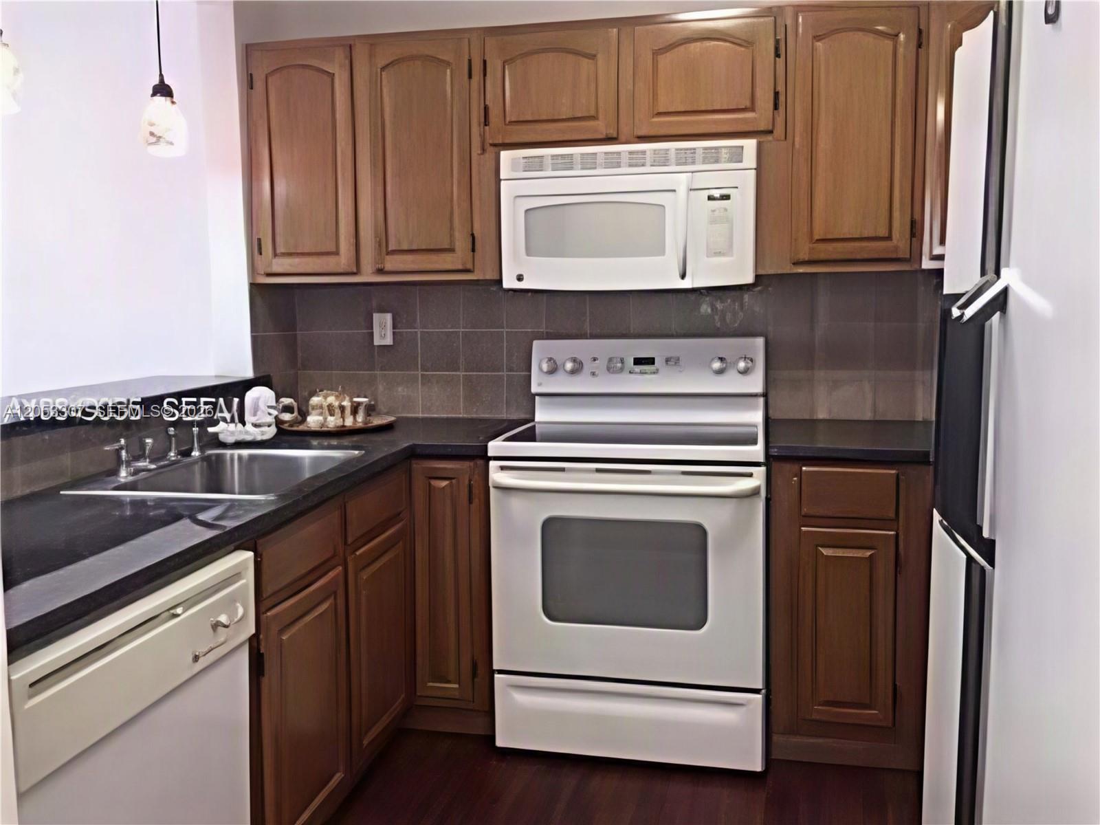 A kitchen features wood cabinets, a white stove, a microwave, and a dark countertop — 8185 NW 7th St. # 101, Miami FL 33126, MIAMI, FL