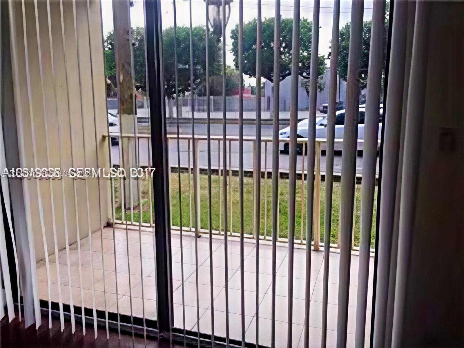 A balcony with tiled flooring and metal railings is viewed through vertical window blinds — 8185 NW 7th St. # 101, Miami FL 33126, MIAMI, FL