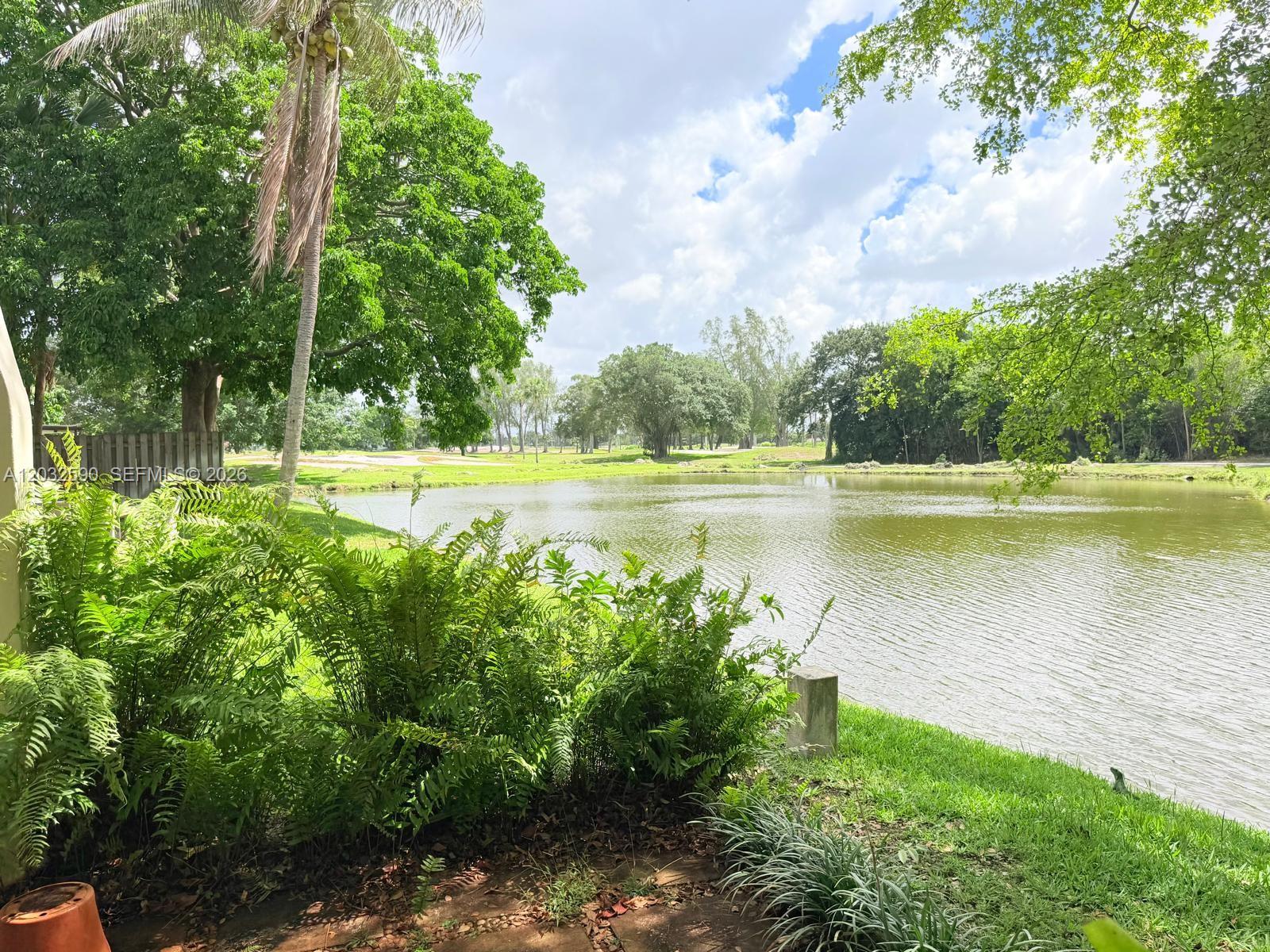 A view of a pond surrounded by lush green trees and landscaping — 18801 Oakland Hills Dr, Hialeah FL 33015, HIALEAH, FL