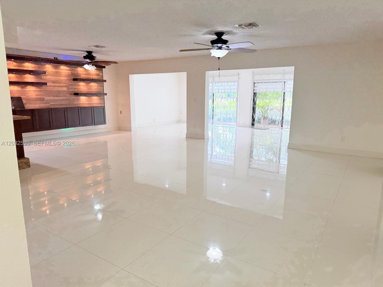 A spacious room features white tile flooring, a wood-paneled accent wall, and ceiling fans — 18801 Oakland Hills Dr, Hialeah FL 33015, HIALEAH, FL