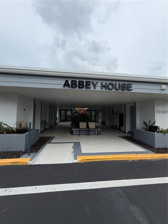 The exterior of a building entrance features a covered walkway with chairs and planters — 21287 GERTRUDE AVENUE UNIT 215, PORT CHARLOTTE, FL
