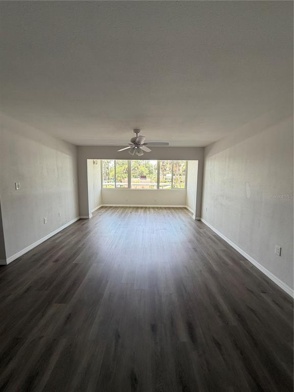 An empty living room features gray wood-look flooring, white walls, and a ceiling fan — 21287 GERTRUDE AVENUE UNIT 215, PORT CHARLOTTE, FL