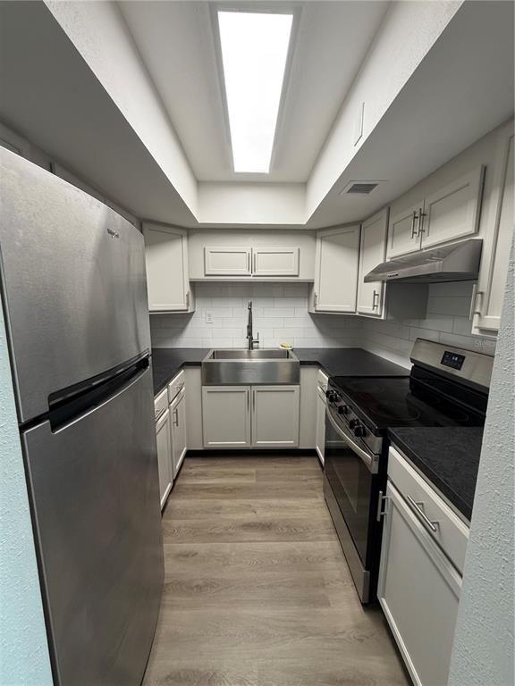 A galley kitchen features stainless steel appliances, white cabinetry, a farmhouse sink, and wood-look flooring — 21287 GERTRUDE AVENUE UNIT 215, PORT CHARLOTTE, FL