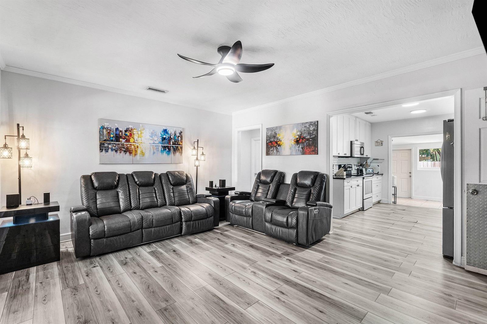 A living room with gray leather recliners, wood-look flooring, and an adjacent white kitchen — 512 36th Street, West Palm Beach FL 33407, WEST PALM BEACH, FL