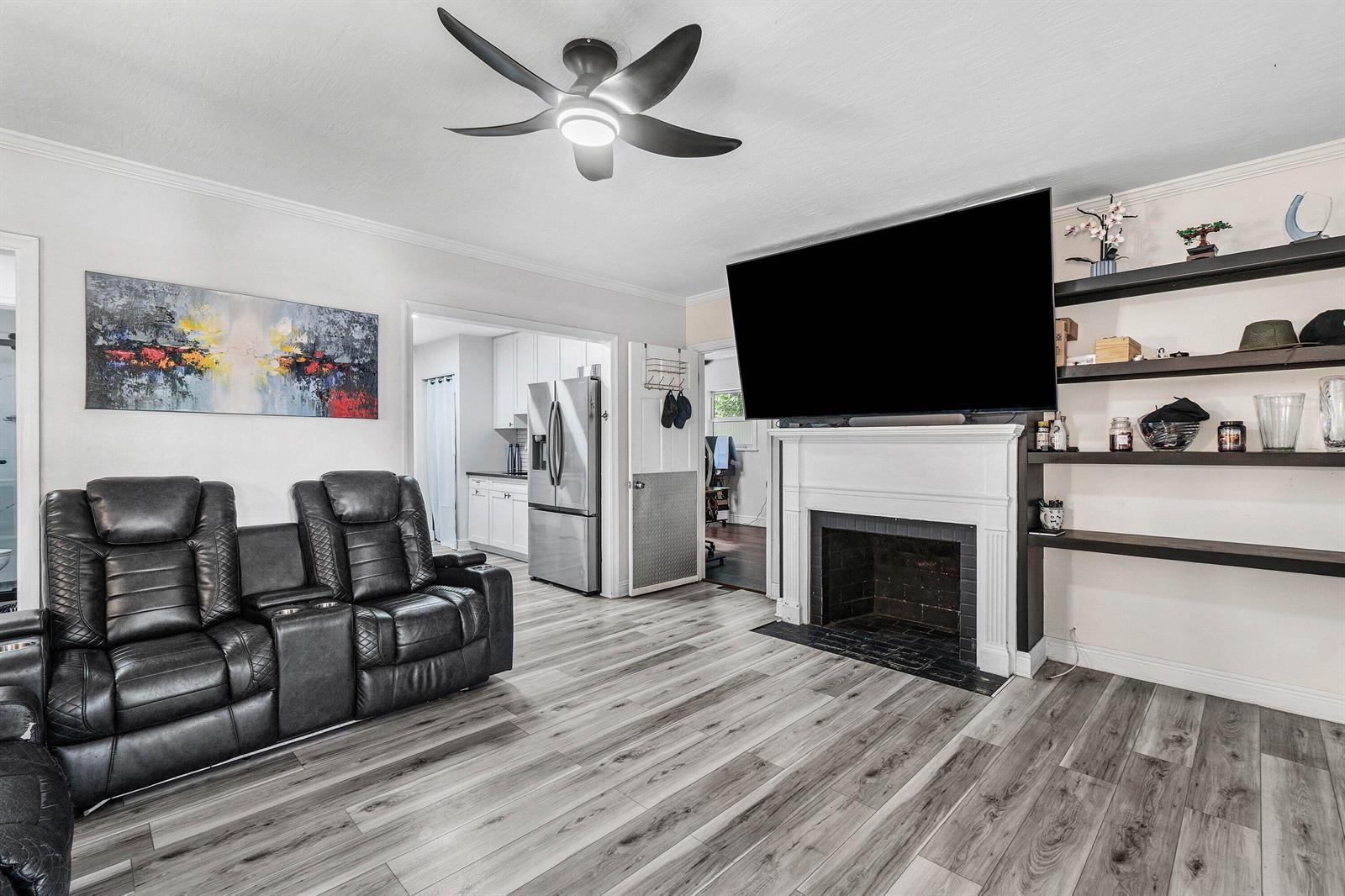 A living room features a fireplace, mounted television, dark shelving, and a black leather sofa — 512 36th Street, West Palm Beach FL 33407, WEST PALM BEACH, FL
