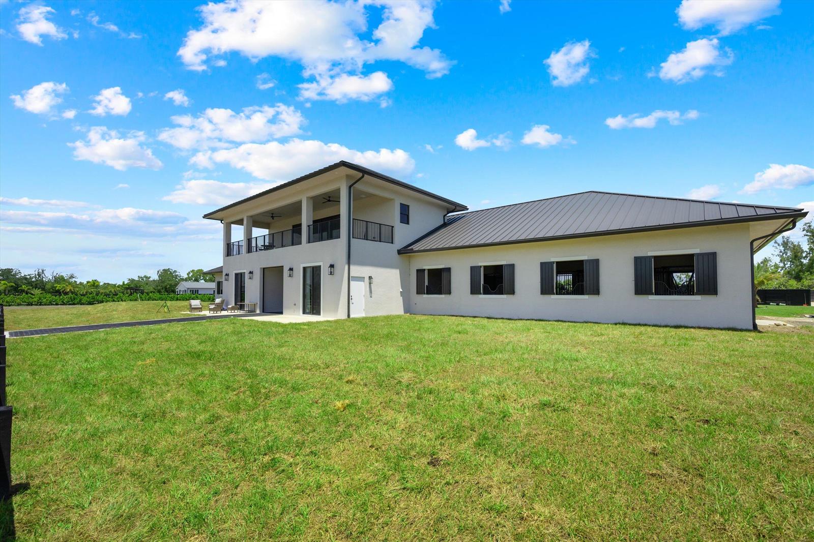 A two-story house with a metal roof and an attached stable wing sits on grass — 16175 Deer Path Lane, Wellington FL 33470, WELLINGTON, FL
