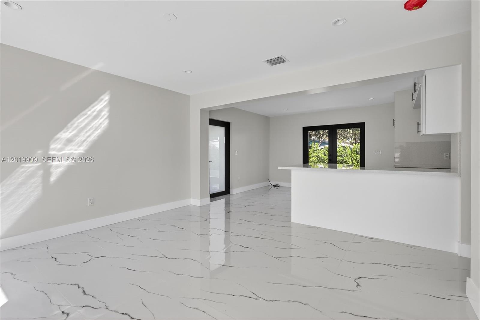 A bright, open-concept living area features white marble-patterned tile flooring and a kitchen breakfast bar — 53 NW 68th St, Miami FL 33150, MIAMI, FL