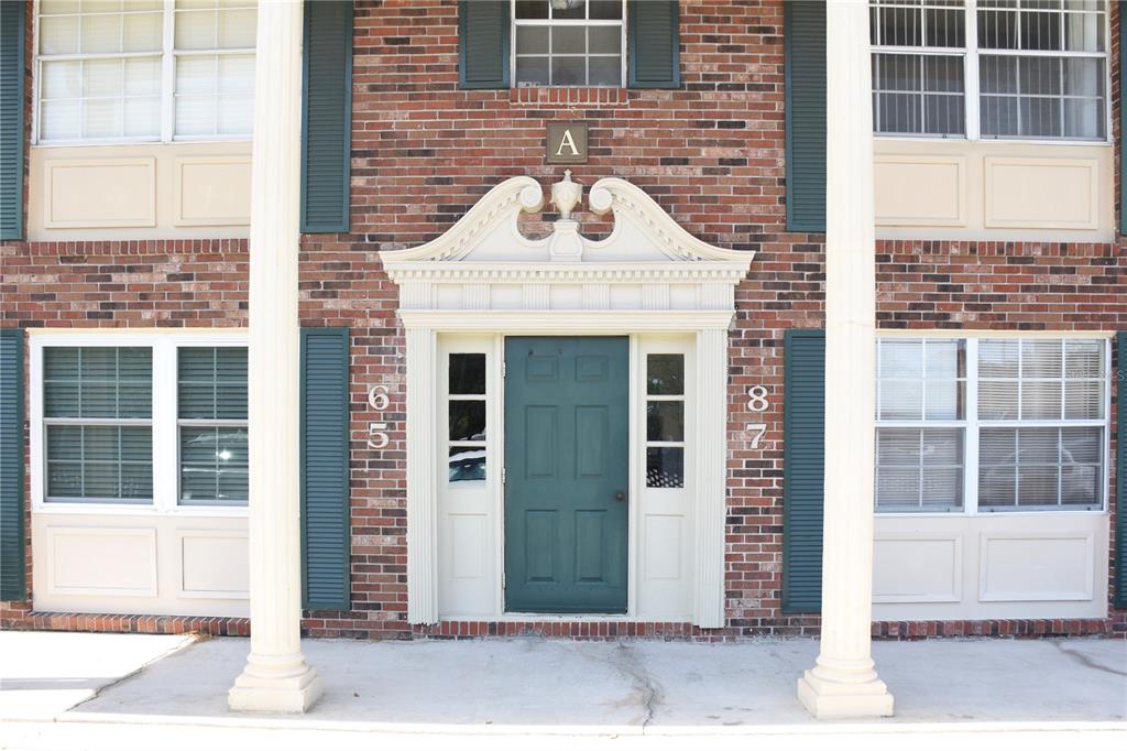 A brick apartment building exterior features a central green door with a decorative white pediment — 1920 E EDGEWOOD DRIVE UNIT A8, LAKELAND, FL