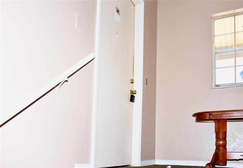 An interior view shows a white door with a lockbox, a handrail, and a wooden table — 1920 E EDGEWOOD DRIVE UNIT A8, LAKELAND, FL