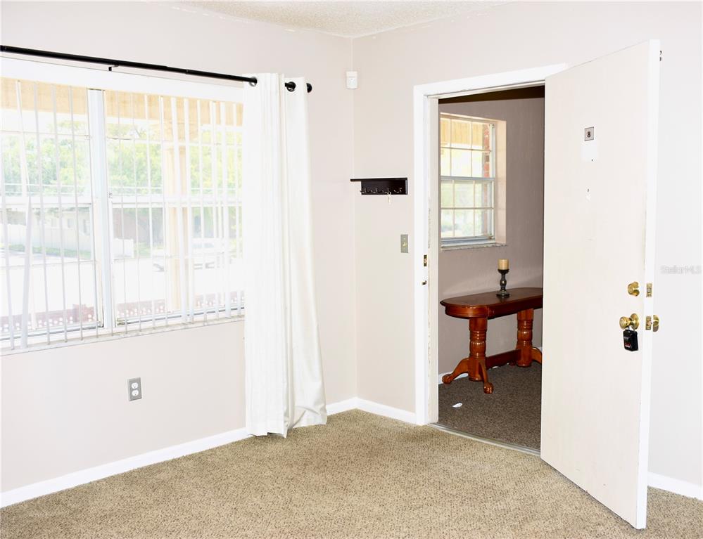 A carpeted room features a large window with white curtains and an open doorway — 1920 E EDGEWOOD DRIVE UNIT A8, LAKELAND, FL