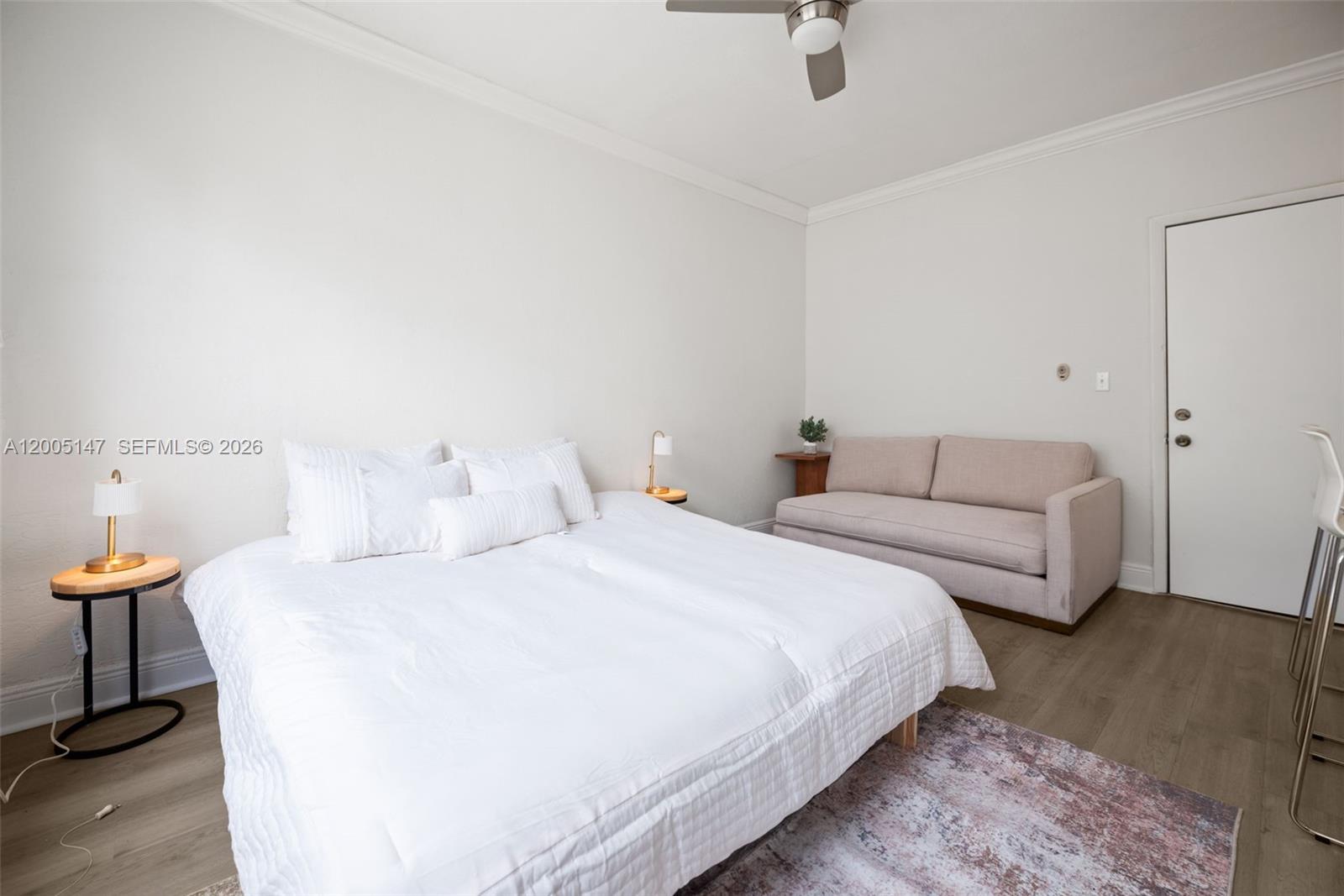 A bedroom features a white bed, a beige sofa, and light wood-look flooring — 119 Menores Ave # 7A, Coral Gables FL 33134, CORAL GABLES, FL