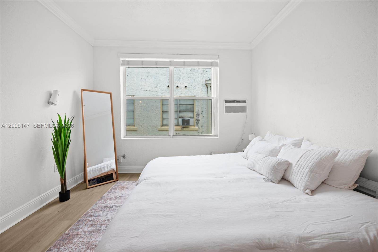A bedroom features a bed with white bedding, a floor mirror, and a window view — 119 Menores Ave # 7A, Coral Gables FL 33134, CORAL GABLES, FL