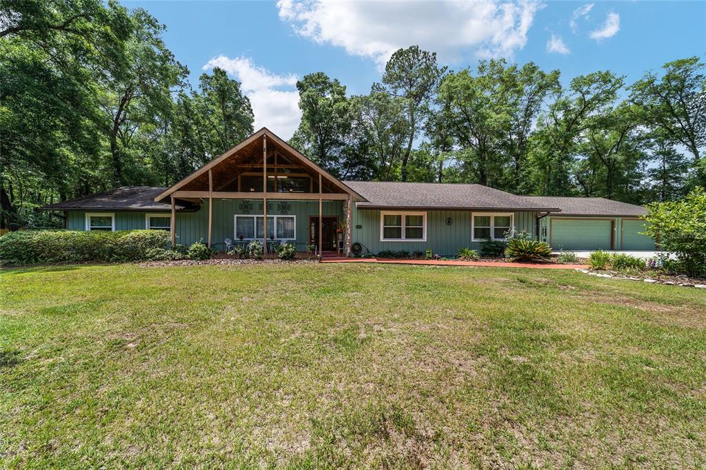 An exterior view of a single-story green house with a large concrete driveway and garage — 5300 NE 2ND LANE, OCALA, FL