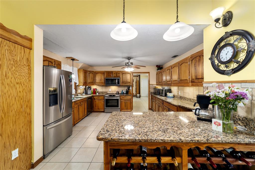 A kitchen with wood cabinets, granite countertops, stainless steel appliances, and a wine rack island — 5300 NE 2ND LANE, OCALA, FL