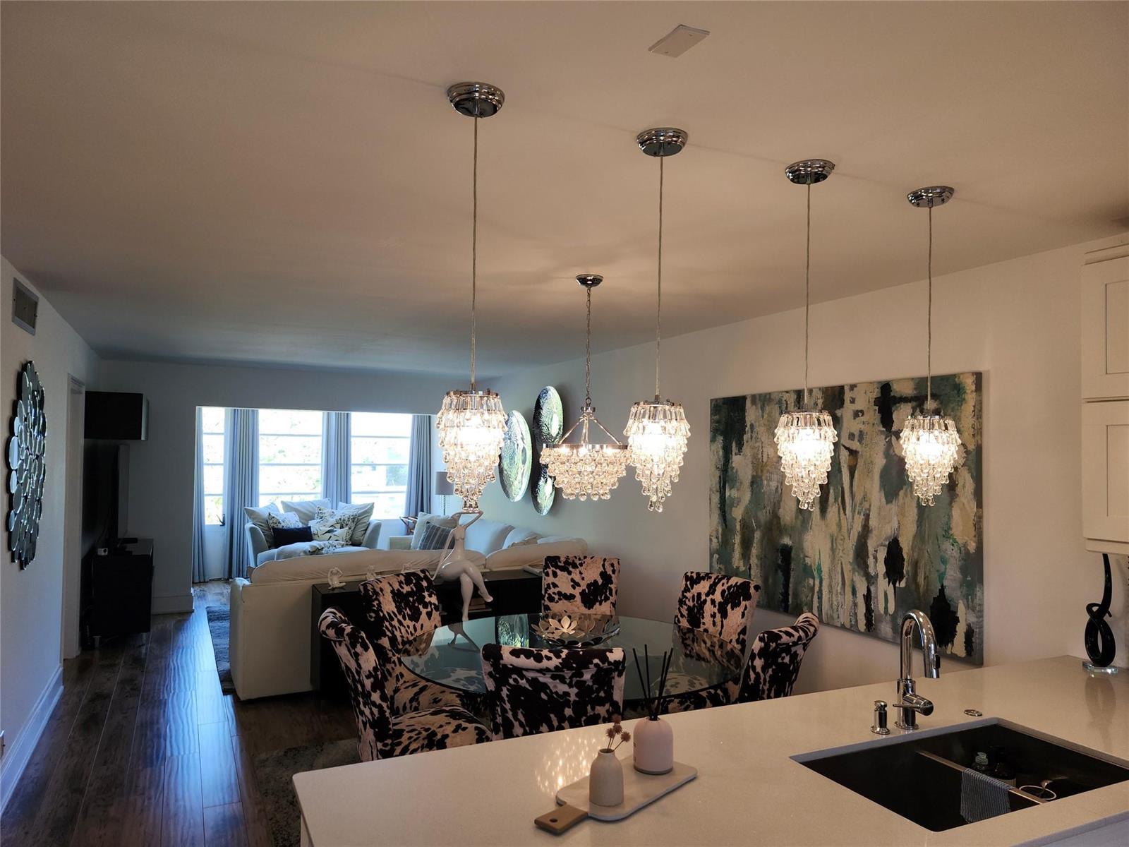 A dining area with a glass table and cow-print chairs sits beneath four crystal pendant lights — 301 Cambridge Road # 301, Hollywood FL 33024, HOLLYWOOD, FL