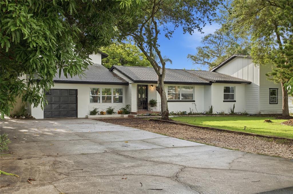A white single-story house with a dark garage door and a concrete driveway — 809 WOODCREST AVENUE, CLEARWATER, FL