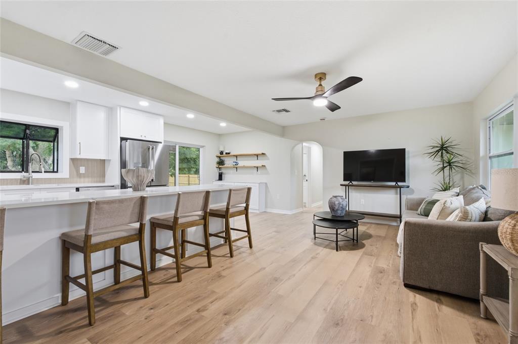 An open-concept kitchen and living area features white cabinetry, a breakfast bar, and wood flooring — 809 WOODCREST AVENUE, CLEARWATER, FL