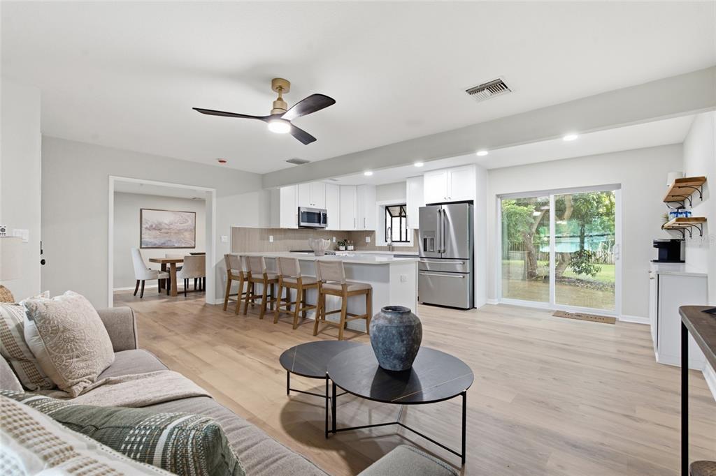 A bright open-concept kitchen and living area features light wood floors and white cabinetry — 809 WOODCREST AVENUE, CLEARWATER, FL