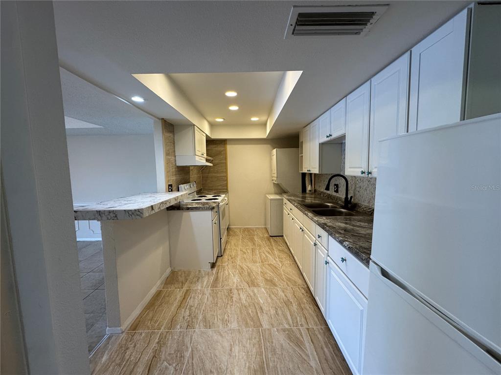 A galley kitchen features white cabinets, dark stone countertops, and light-colored tile flooring — 4575 S TEXAS AVENUE UNIT 109, ORLANDO, FL