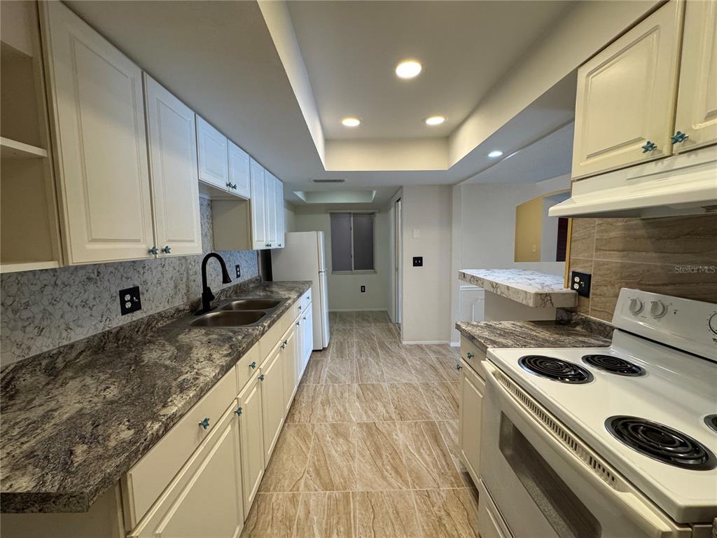 A kitchen features white cabinets, granite countertops, a double sink, and light-colored tile flooring — 4575 S TEXAS AVENUE UNIT 109, ORLANDO, FL