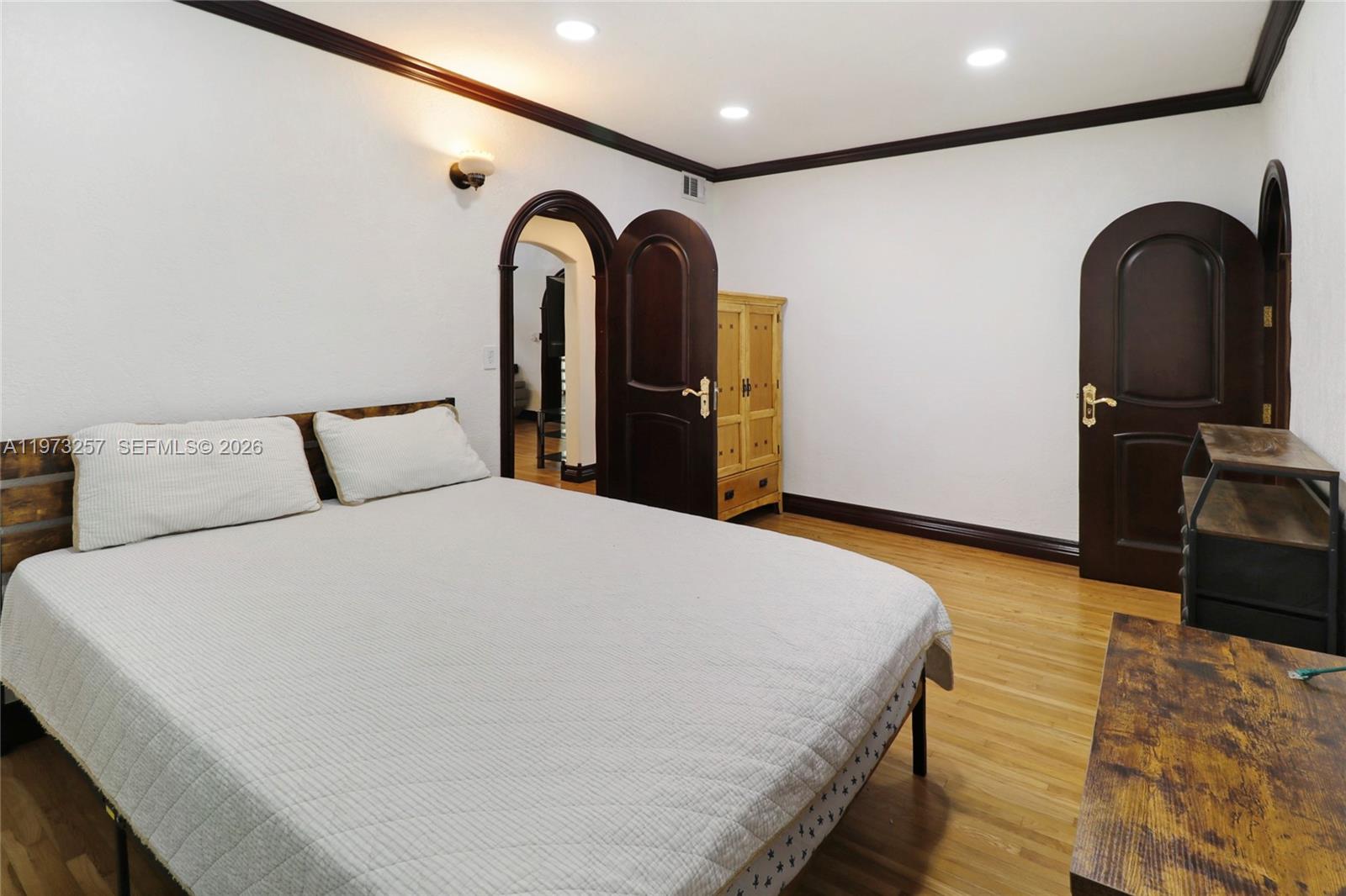 A bedroom features a bed, hardwood floors, dark wood trim, and arched doorways — 550 Quail Ave, Miami Springs FL 33166, MIAMI SPRINGS, FL