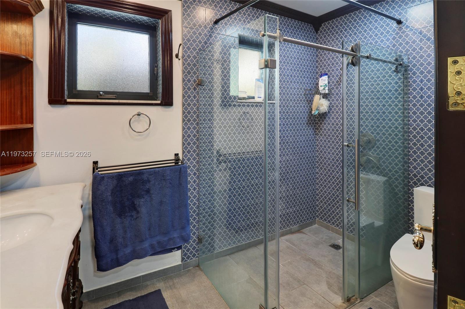 A bathroom features a glass-enclosed shower with blue patterned tile and a white vanity — 550 Quail Ave, Miami Springs FL 33166, MIAMI SPRINGS, FL