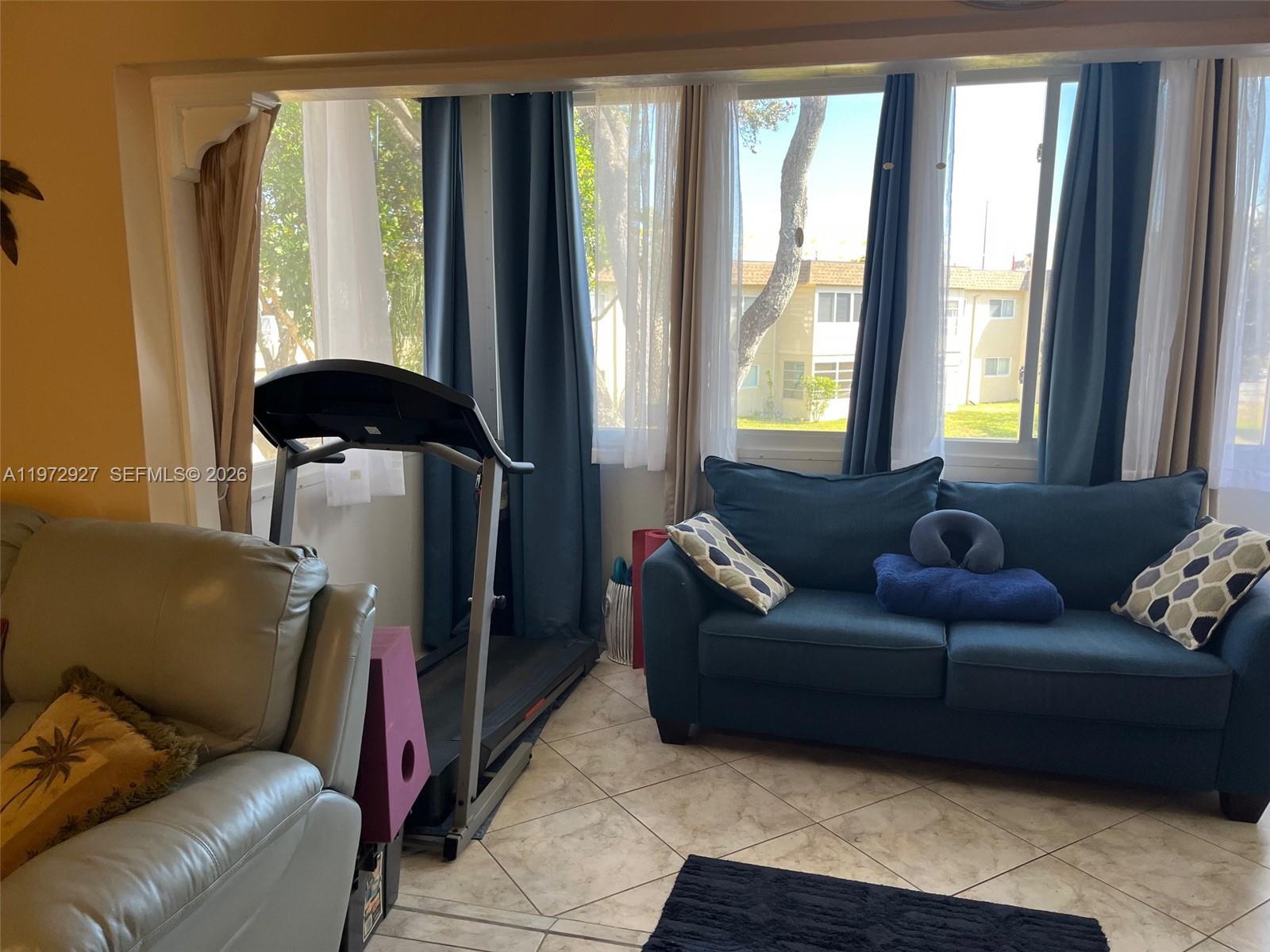 A sunroom features tile flooring, a treadmill, and a blue sofa in front of windows — 752 Lori Dr # 218, Palm Springs FL 33461, PALM SPRINGS, FL