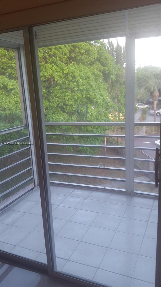 A view from inside looking out through sliding glass doors onto a tiled balcony — 4384 NW 9th Ave # 3B, Deerfield Beach FL 33064, DEERFIELD BEACH, FL