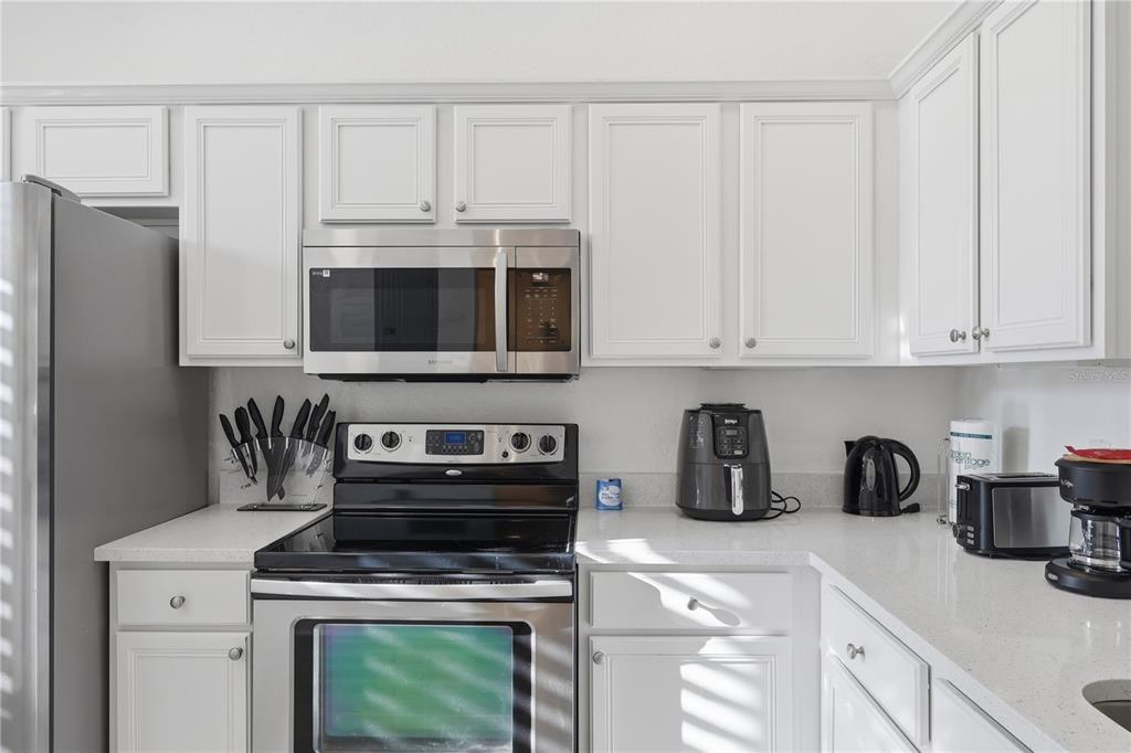 A kitchen features white cabinets, stainless steel appliances, and light-colored quartz countertops — 3438 CALABRIA AVENUE UNIT 3438, DAVENPORT, FL