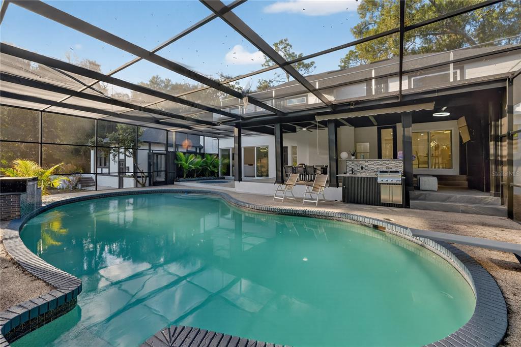 A swimming pool sits inside a screened-in patio area with an outdoor kitchen and seating — 305 SWEETWATER CLUB CIRCLE, LONGWOOD, FL